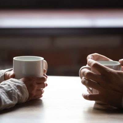 Close up woman and man sitting in cafe, holding warm cups of coffee on table, young couple spending weekend in cozy coffeehouse together, romantic date concept, visitors drinking hot beverages
