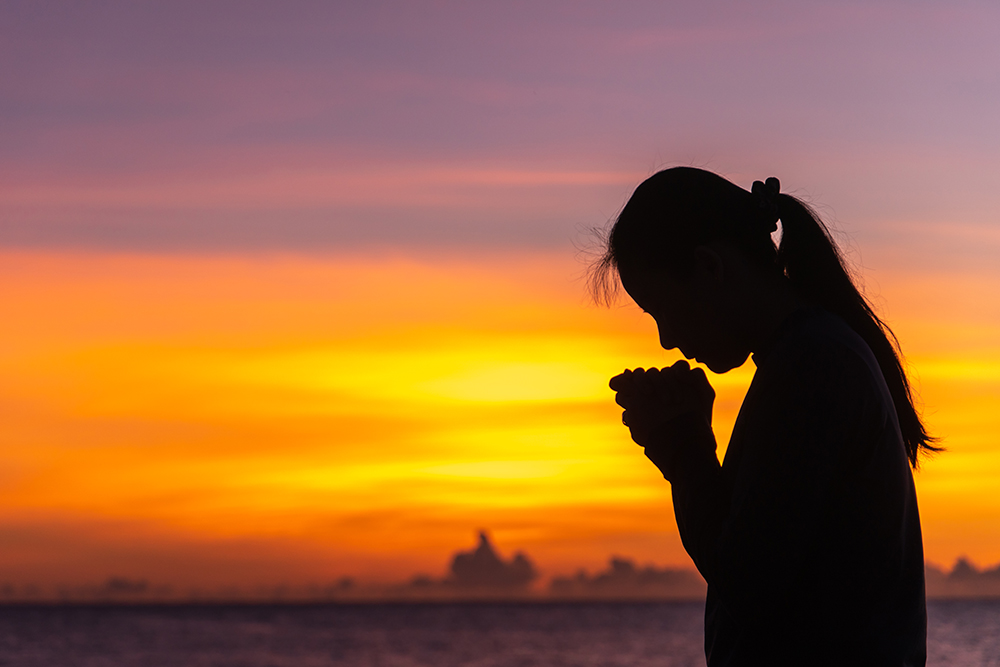 Silhouette of woman praying at sunrise