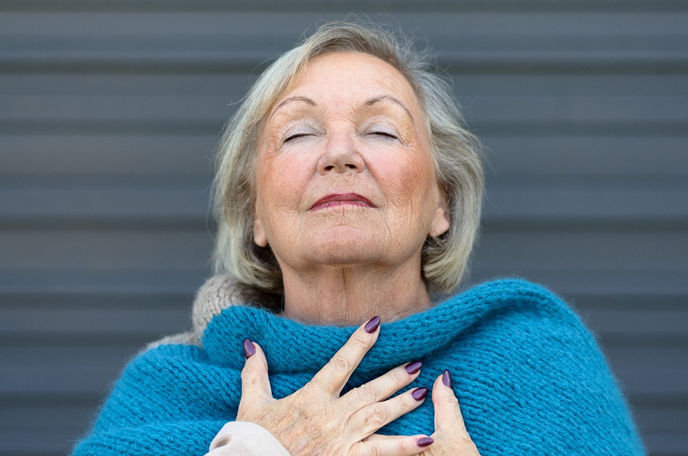 Serene older woman breathes deeply with her palms on her chest and her eyes closed