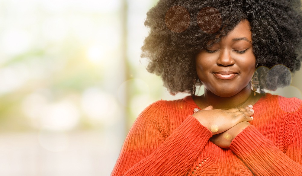 African woman with curly hair smiling with hands on her heart